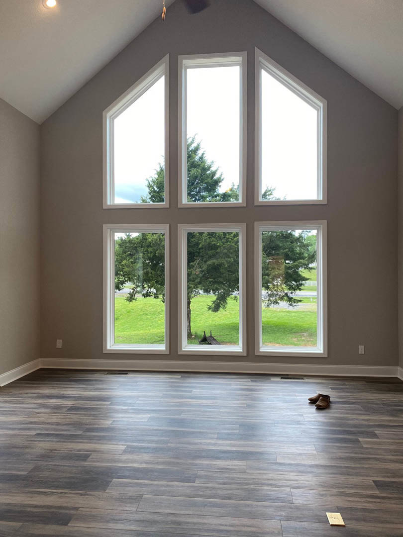 Spacious room featuring wide wood flooring, crisp white walls, and a wall of large windows overlooking green trees and grass