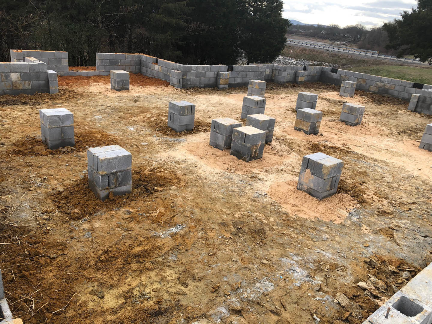 Stacked grey cement blocks on dirt at a residential construction site with trees and sky in the background