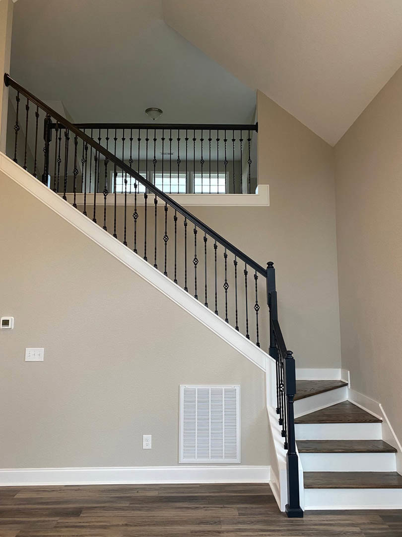 Black metal railing on staircase with light wood treads, white walls, and white ceiling