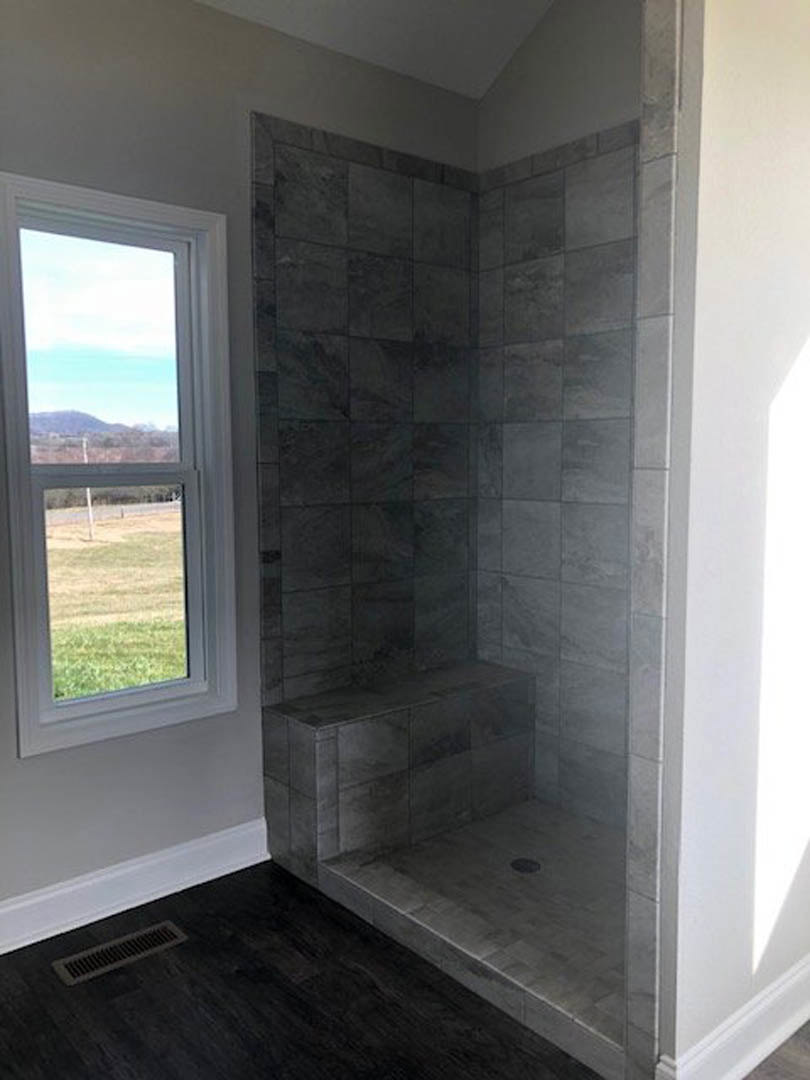 Grey tiled shower stall with glass enclosure, stone step, and window overlooking field and mountains