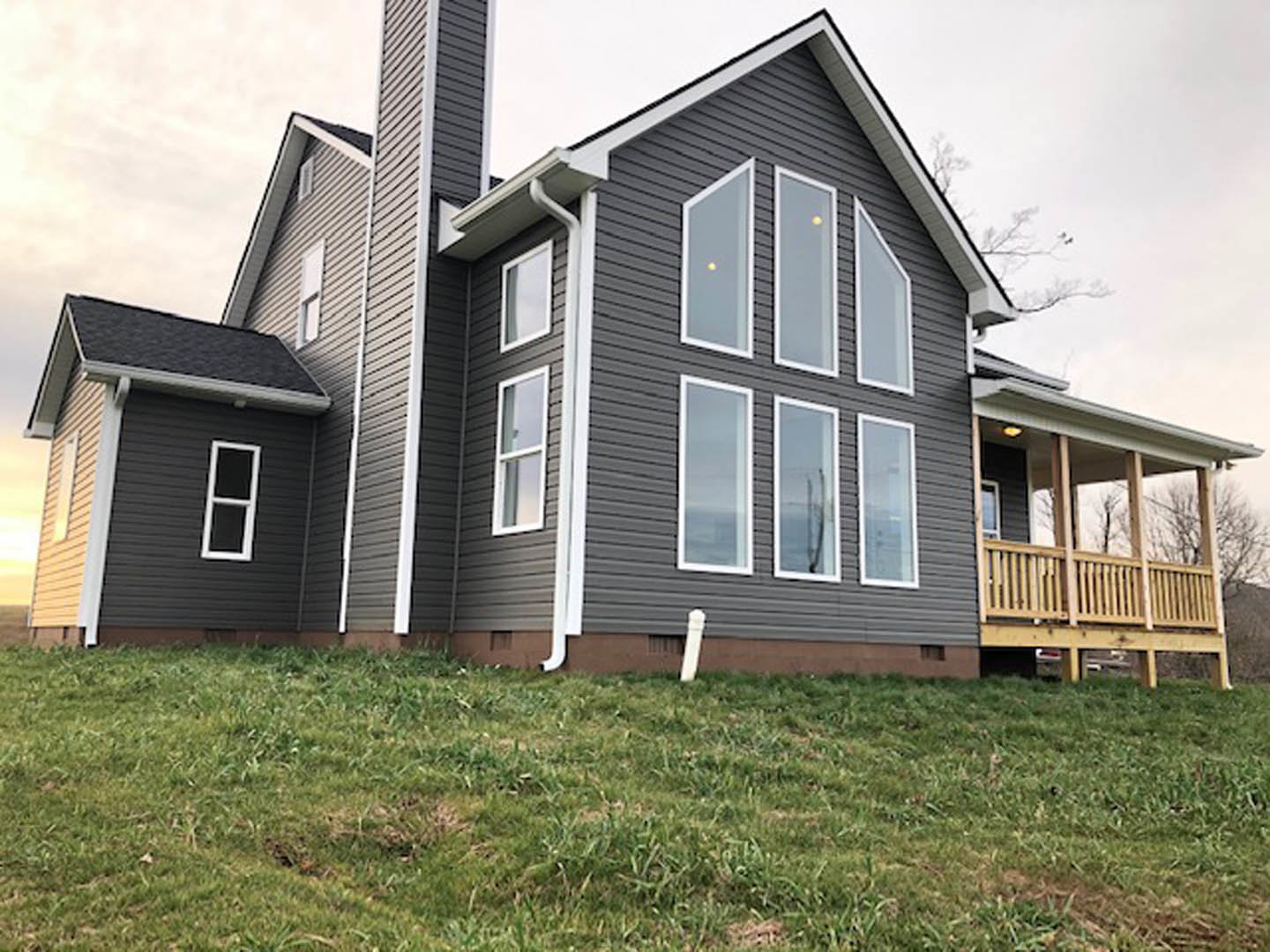 Two-story home with white siding, wooden porch and deck, white-framed windows, grassy lawn, and yellow ball suspended above the yard