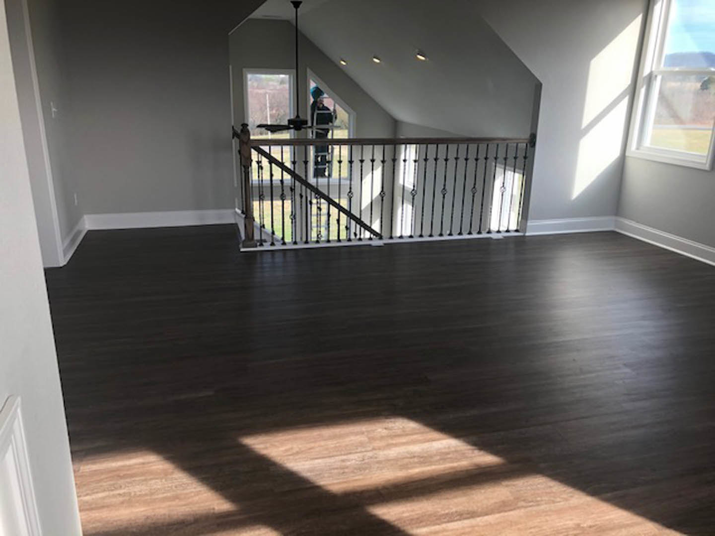 Open room with light wood flooring, modern metal railing along staircase, white walls, large window letting in natural light