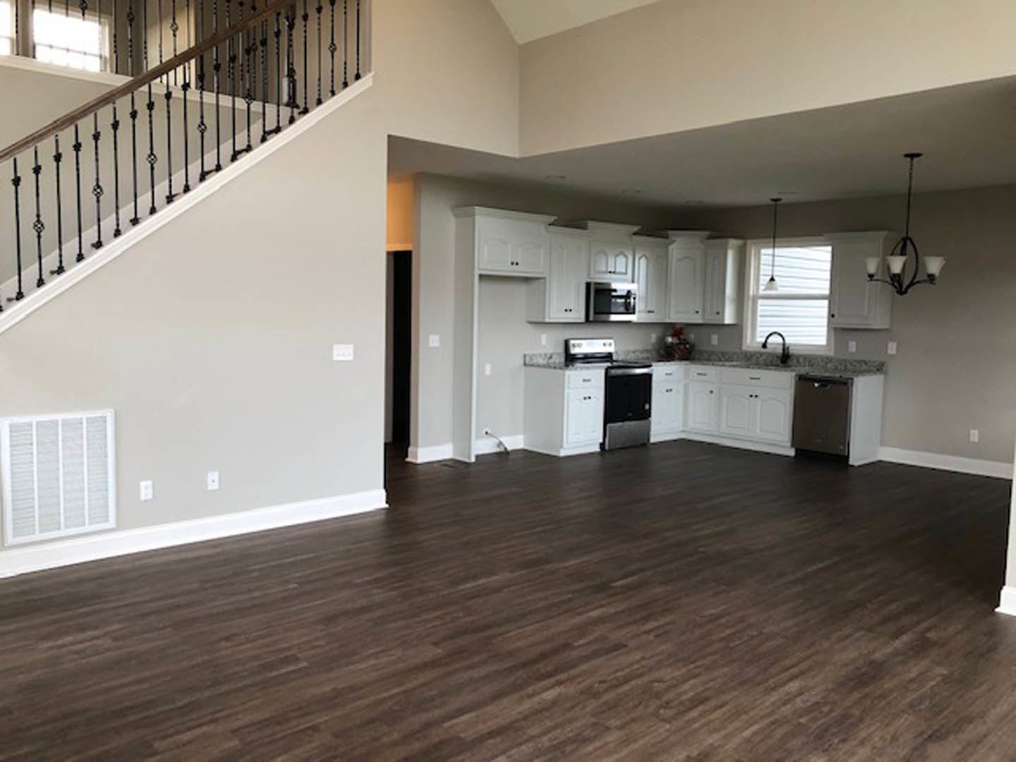 Open kitchen and dining area with hardwood floors, white cabinetry with black drawers, modern chandelier, staircase with wood treads, and a person seated at the dining table.