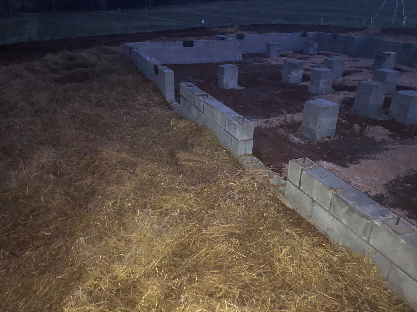 Concrete block foundation set on grassy field with exposed soil, surrounded by open outdoor landscape.