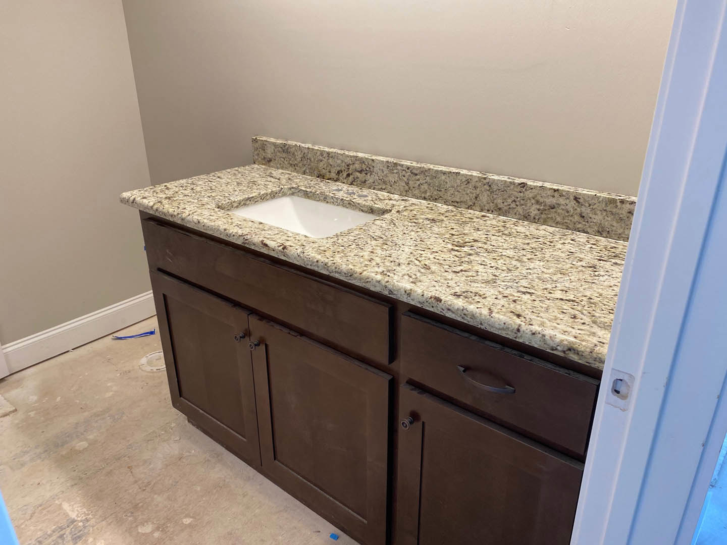 Granite bathroom countertop with white undermount sink, chrome faucet, tile backsplash, and wood cabinetry