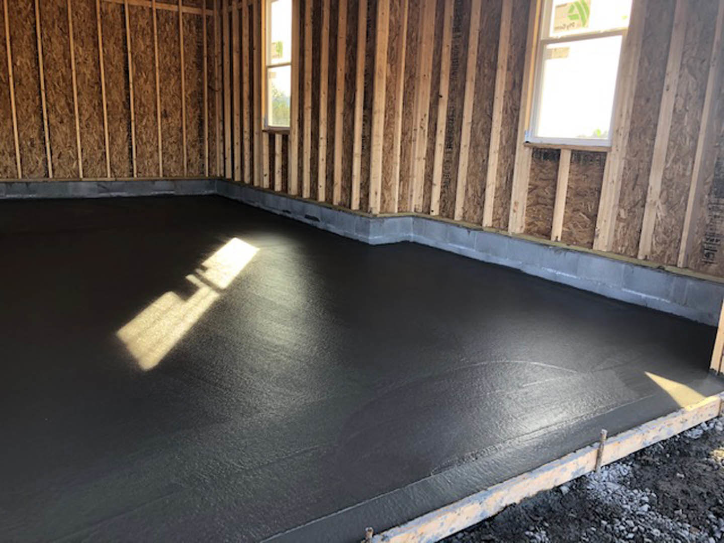 Concrete black floor with sunlight streaming through window, wood-paneled walls, and exposed wooden framing in a garage or interior room