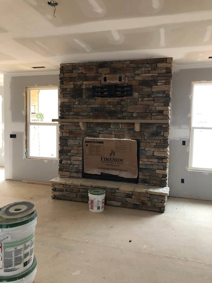 Brick fireplace with white plaster walls, cardboard box and white bucket with green lid on wood floor, window in background