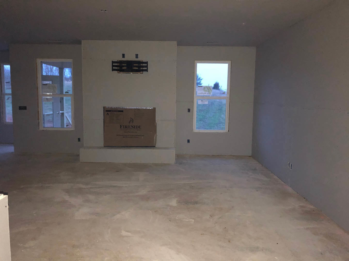 Bright room with white plaster walls, white flooring, large window displaying outdoor view, wall-mounted box with text, and modern fireplace.