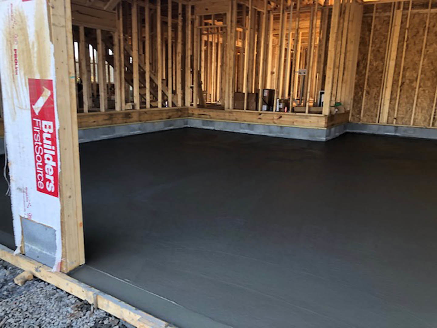Smooth concrete floor in unfinished room with exposed wood framing, red and white construction sign, and a dog lying on the ground