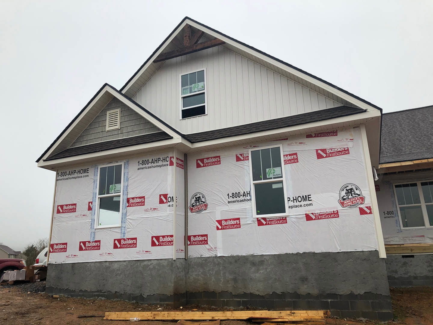 White siding exterior with red construction tape, plastic covering partially visible, window featuring a sign, white vent, and wooden board detail.