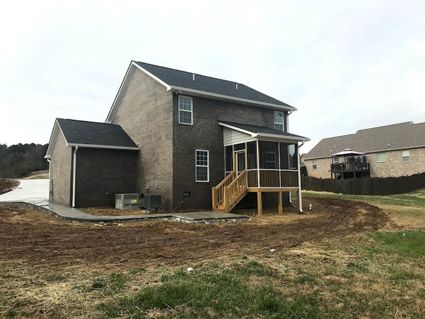 White cottage-style home with covered front porch, wooden railing, and picket fence, surrounded by green lawn and shrubs under blue sky