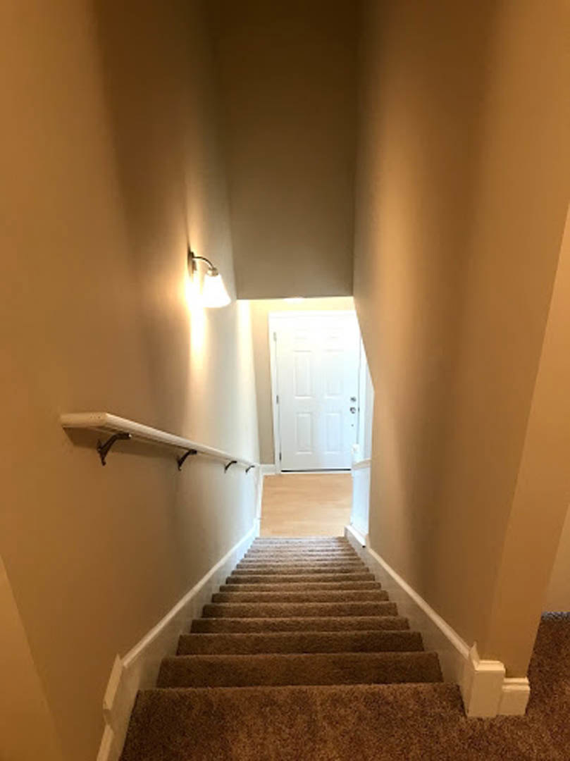 Wood staircase with metal handrail, plaster walls, wall-mounted sconce, light hardwood flooring, white ceiling