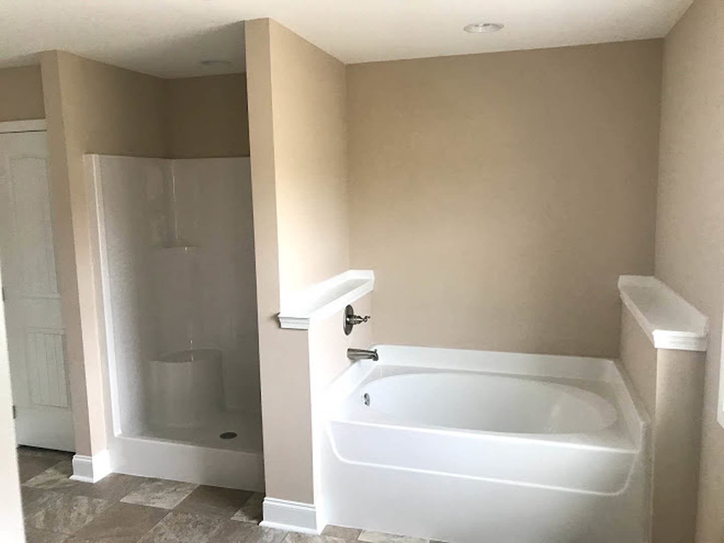 Bathroom with white tile walls, freestanding white bathtub with silver faucet, glass-enclosed shower, and recessed lighting