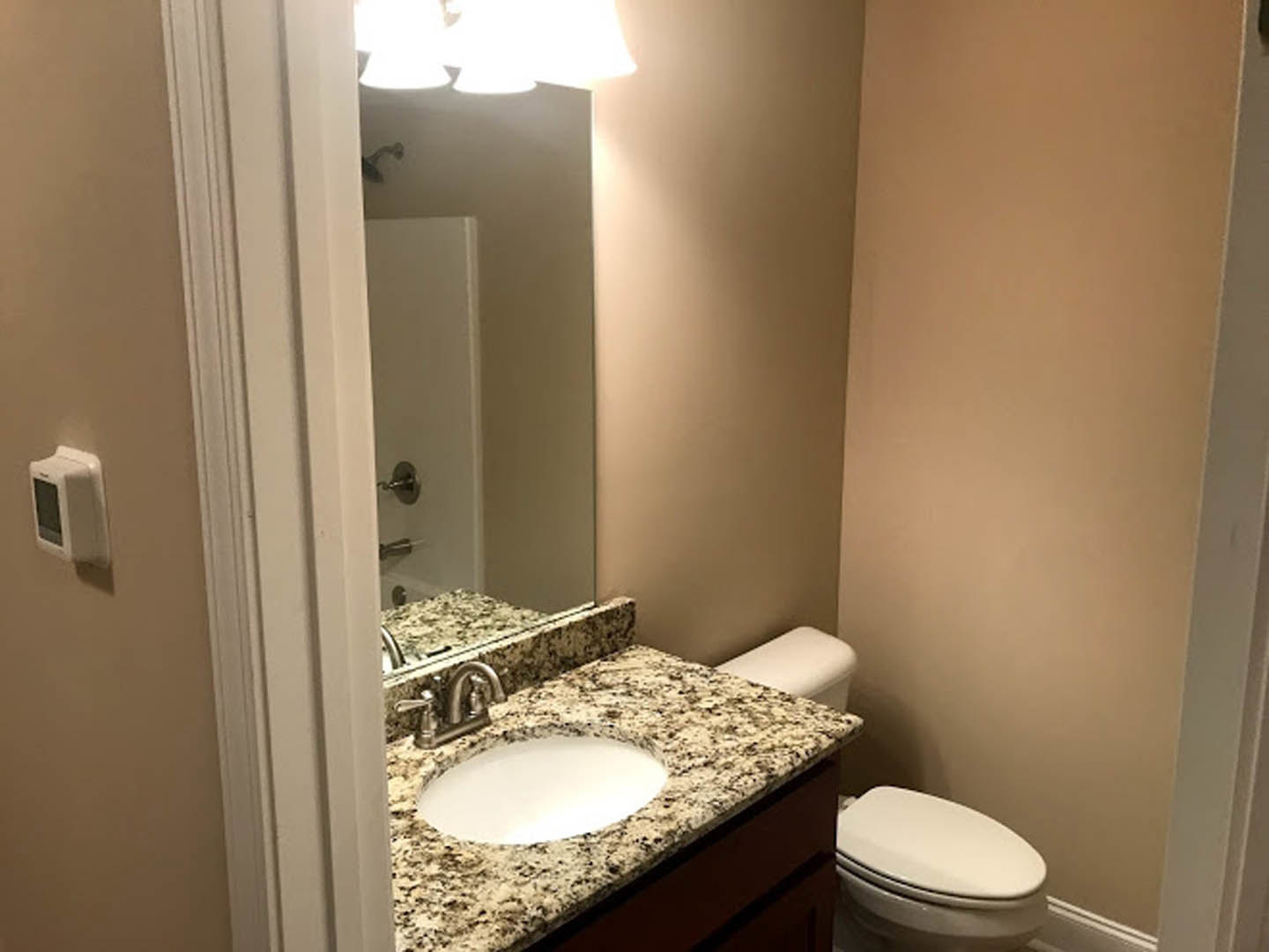 Marble countertop with undermount sink, chrome faucet, white toilet, light tile flooring, neutral wall tiles, soft natural lighting