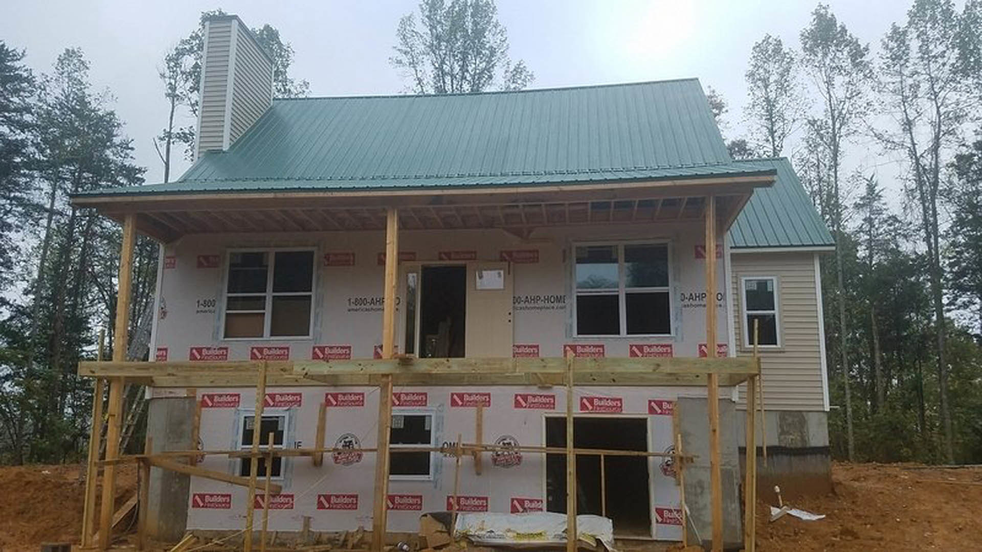Wood-framed house under construction with green roof, exposed beams, window opening, and red construction signs on exterior