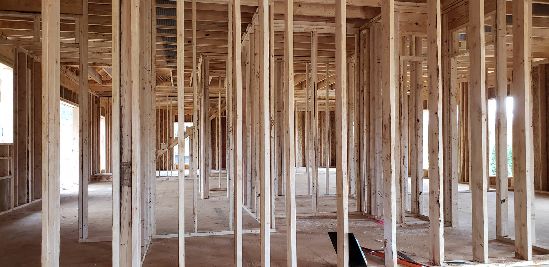 Exposed wood framing and beams inside a partially constructed room, laptop on a makeshift surface, white post with rust, soft light filtering through unfinished walls