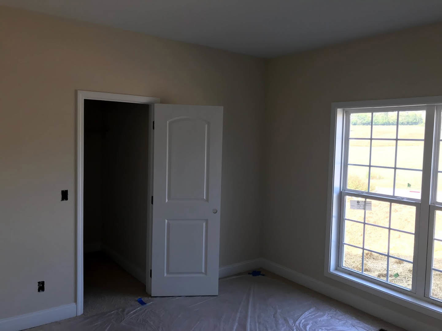 White-walled room featuring an open white door with a round knob, large window with a sign, and light-colored flooring.