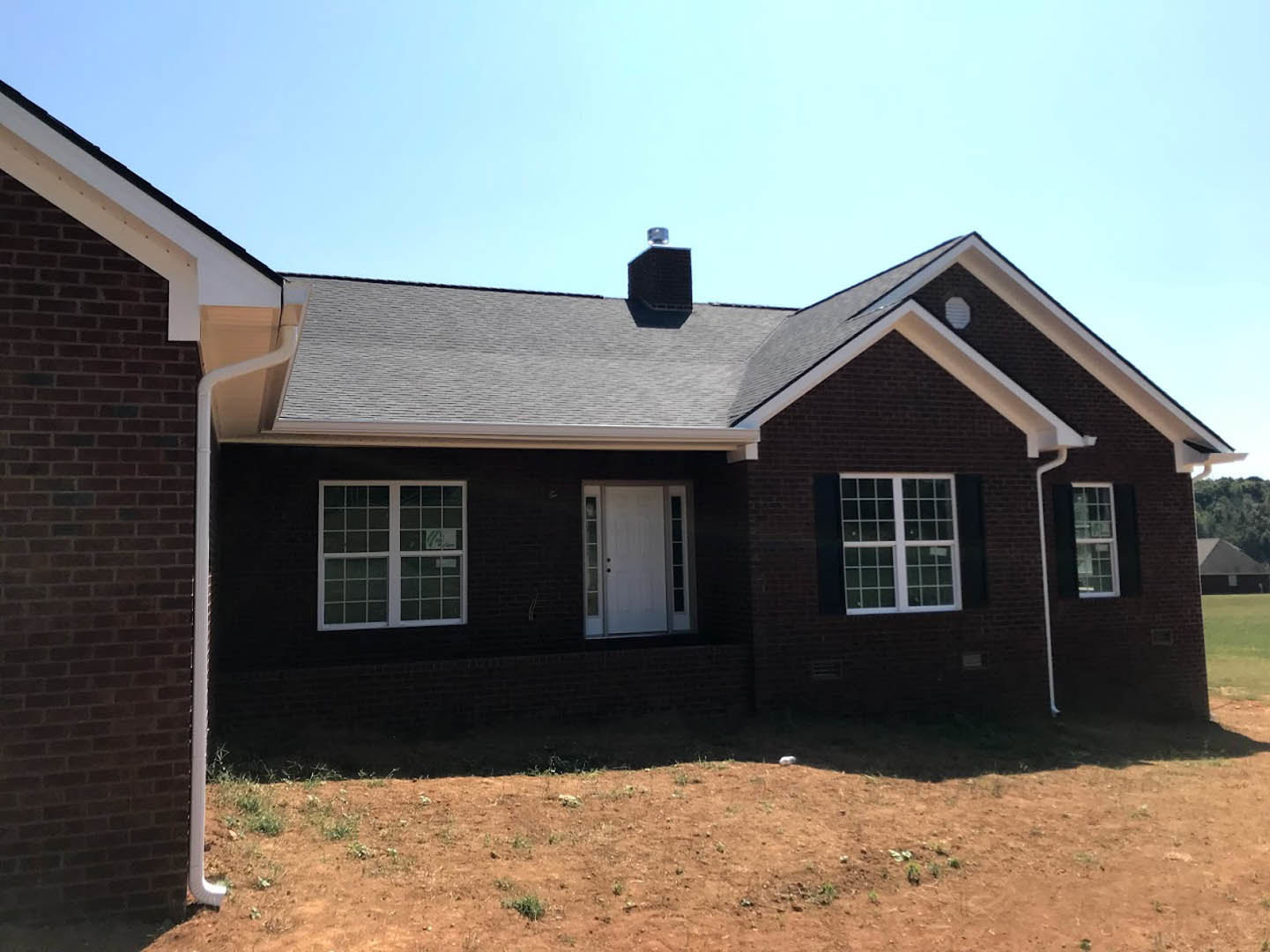 Two-story house with white siding, multi-pane windows, and glass-paneled front door, set on a dirt yard with a small white bird perched on a hill.