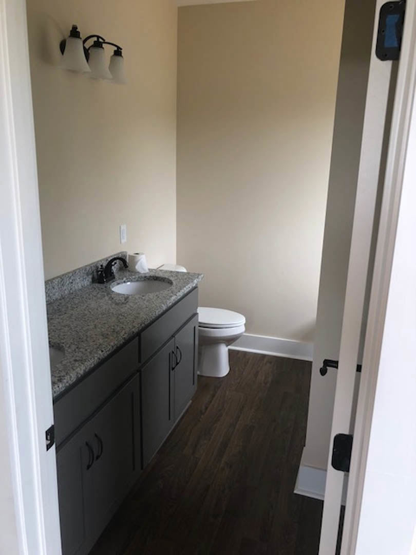 Marble countertop with black faucet, white sink, toilet, dark wood flooring, three-shade light fixture, and white cabinetry in a bathroom.