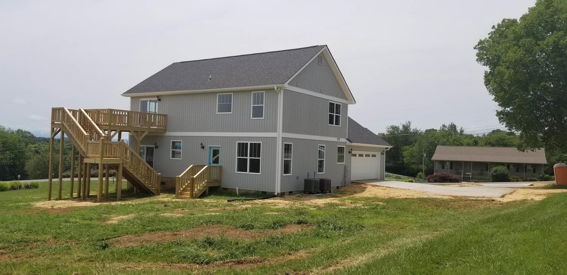 Grey siding house with blue front door, wooden porch stairs, white-framed windows, green lawn, concrete driveway, and open sky above