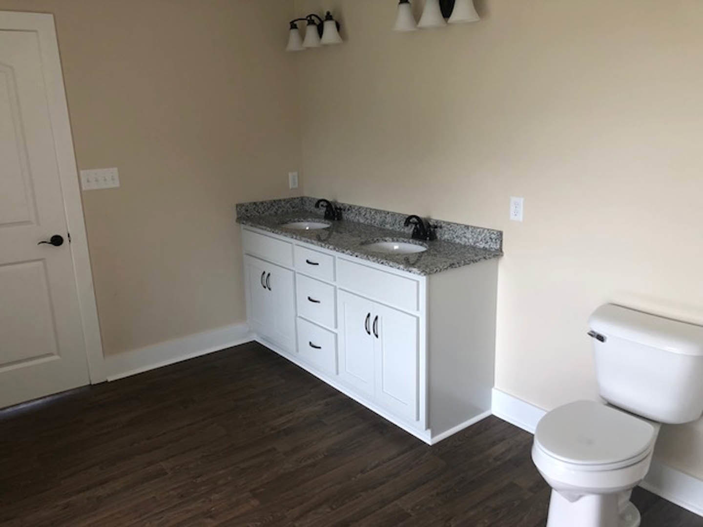 Bathroom with marble countertop, undermount sink, white toilet beside tiled wall, chrome faucet, light fixture with white shade, neutral cabinetry, and tile flooring.