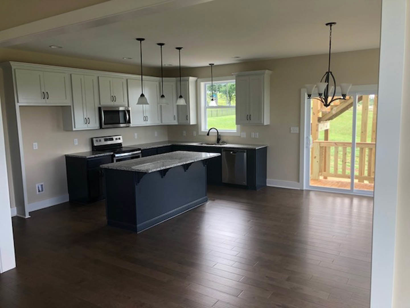 Kitchen with dark wood flooring, blue accent wall, marble-topped island, stainless steel stove and microwave, white cabinetry, and undermount sink