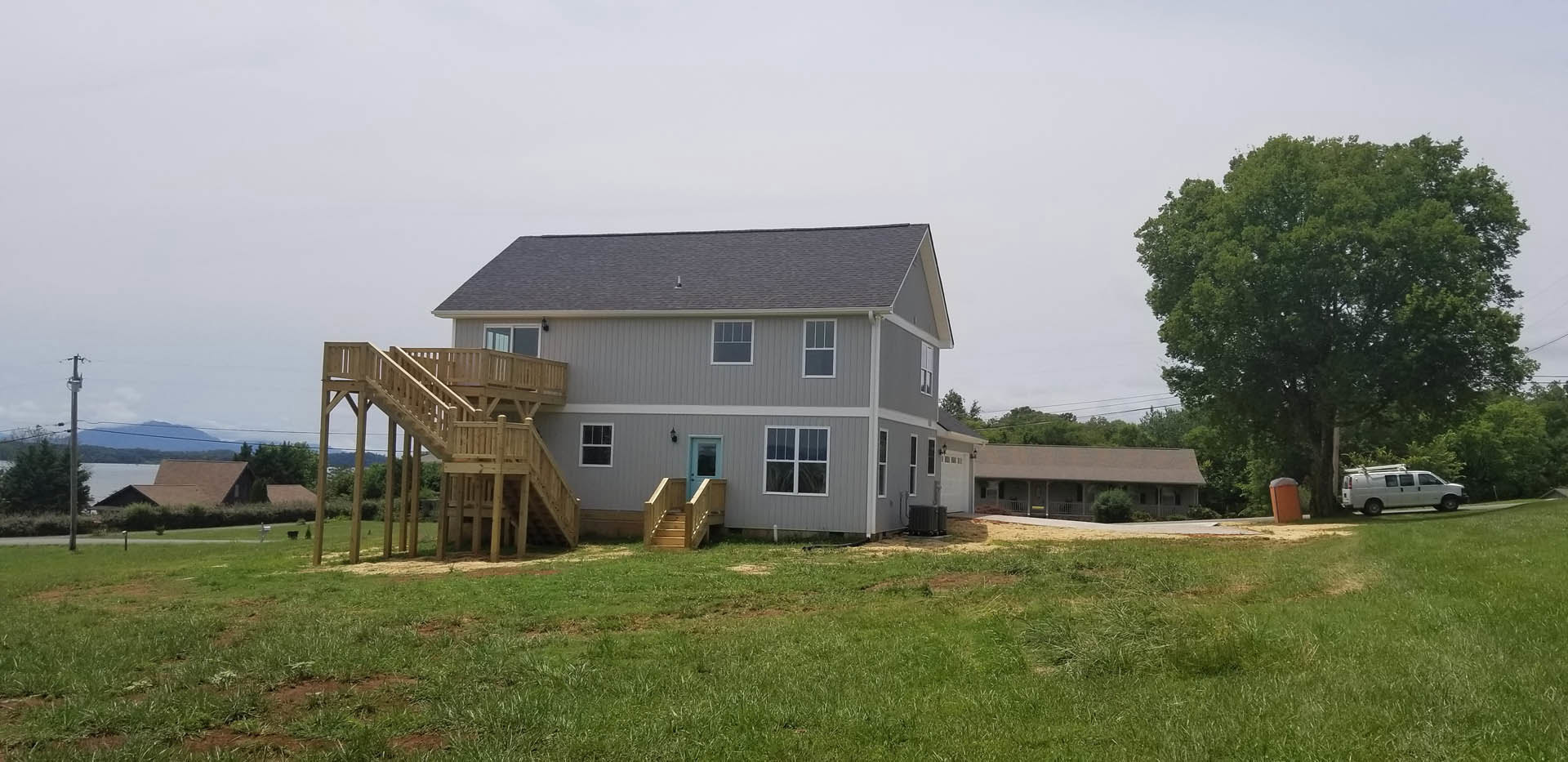 Two-story house with blue front door, wooden exterior stairs, attached garage, large grassy yard, mature tree, and white van parked in driveway