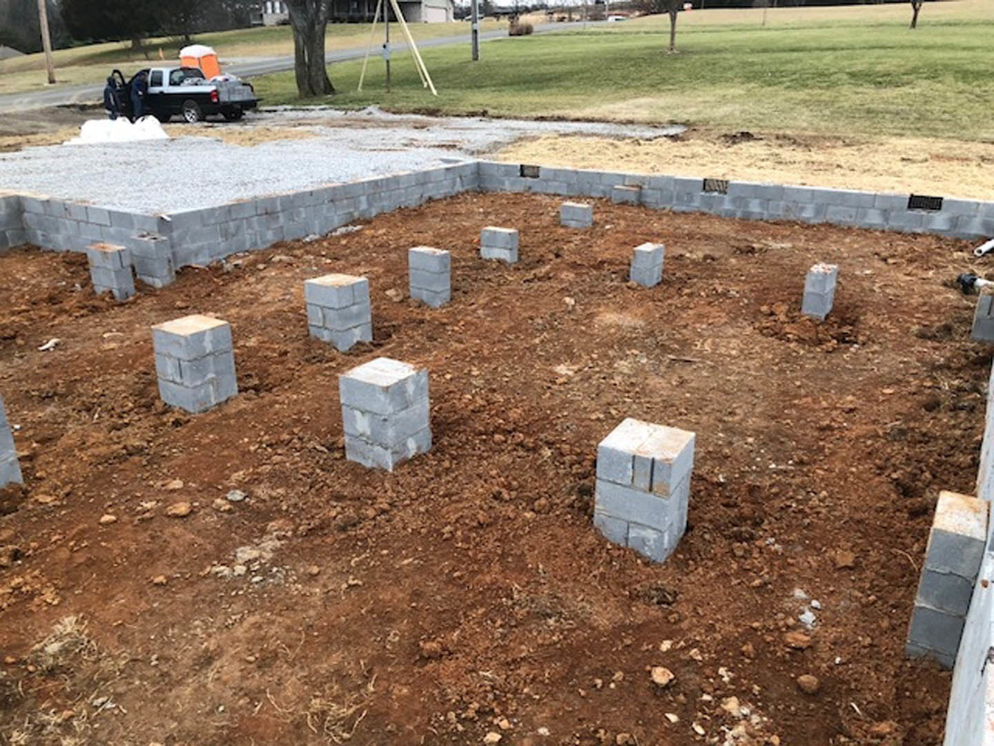 Concrete blocks set into soil with patches of grass, white brick wall and brown pole in background, black and white truck parked nearby.