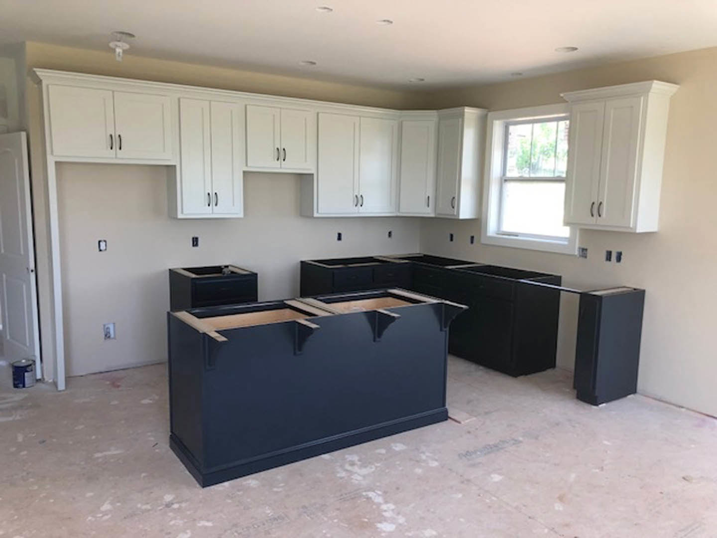 White kitchen cabinets with black countertops, stainless steel sink, white-framed window, black cabinet drawers, and white door with black knobs