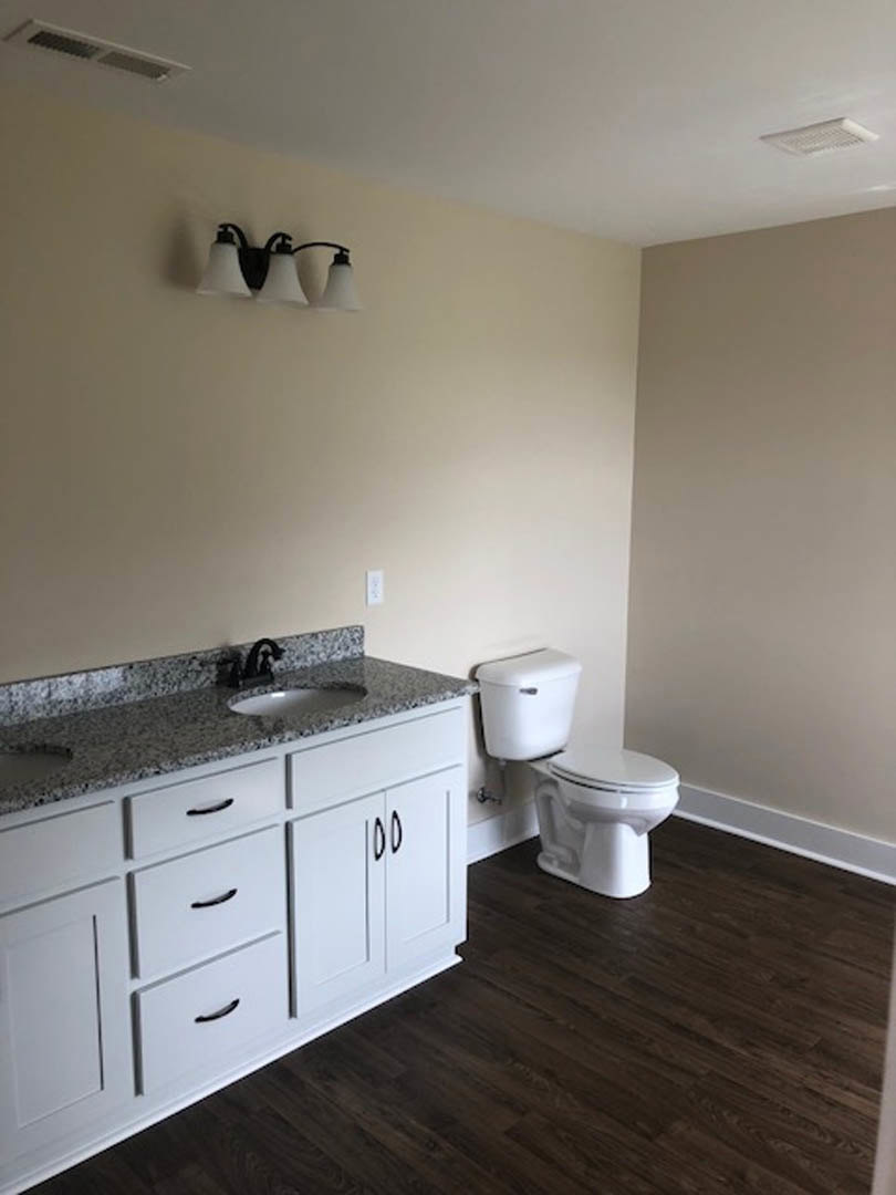 Marble countertop with undermount sink, white vanity cabinet, chrome faucet, white toilet, dark wood flooring, tile backsplash, modern light fixture