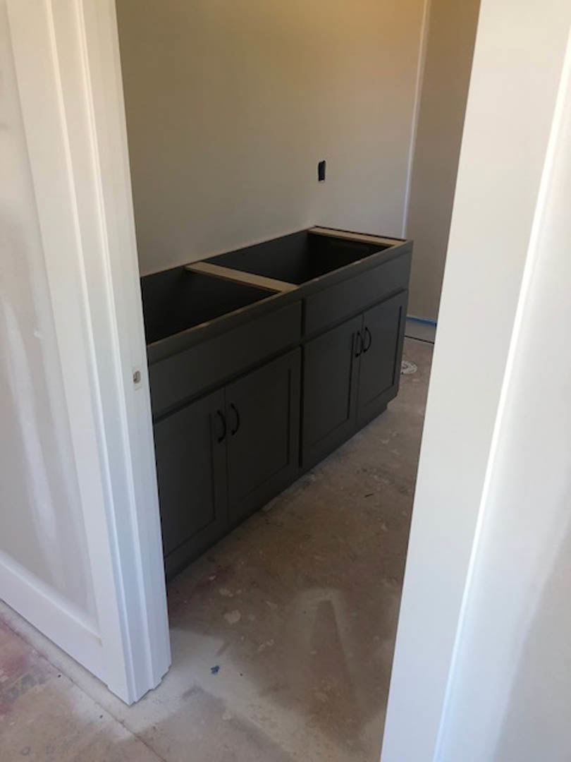 Black kitchen cabinets with white drawer fronts, white walls, tile flooring, and a stone countertop in a modern indoor space.