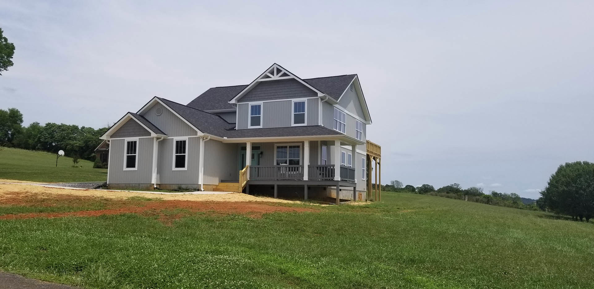 Two-story home with white-framed windows, covered front porch, expansive green lawn, mature tree, and metal posts bordering grassy field.