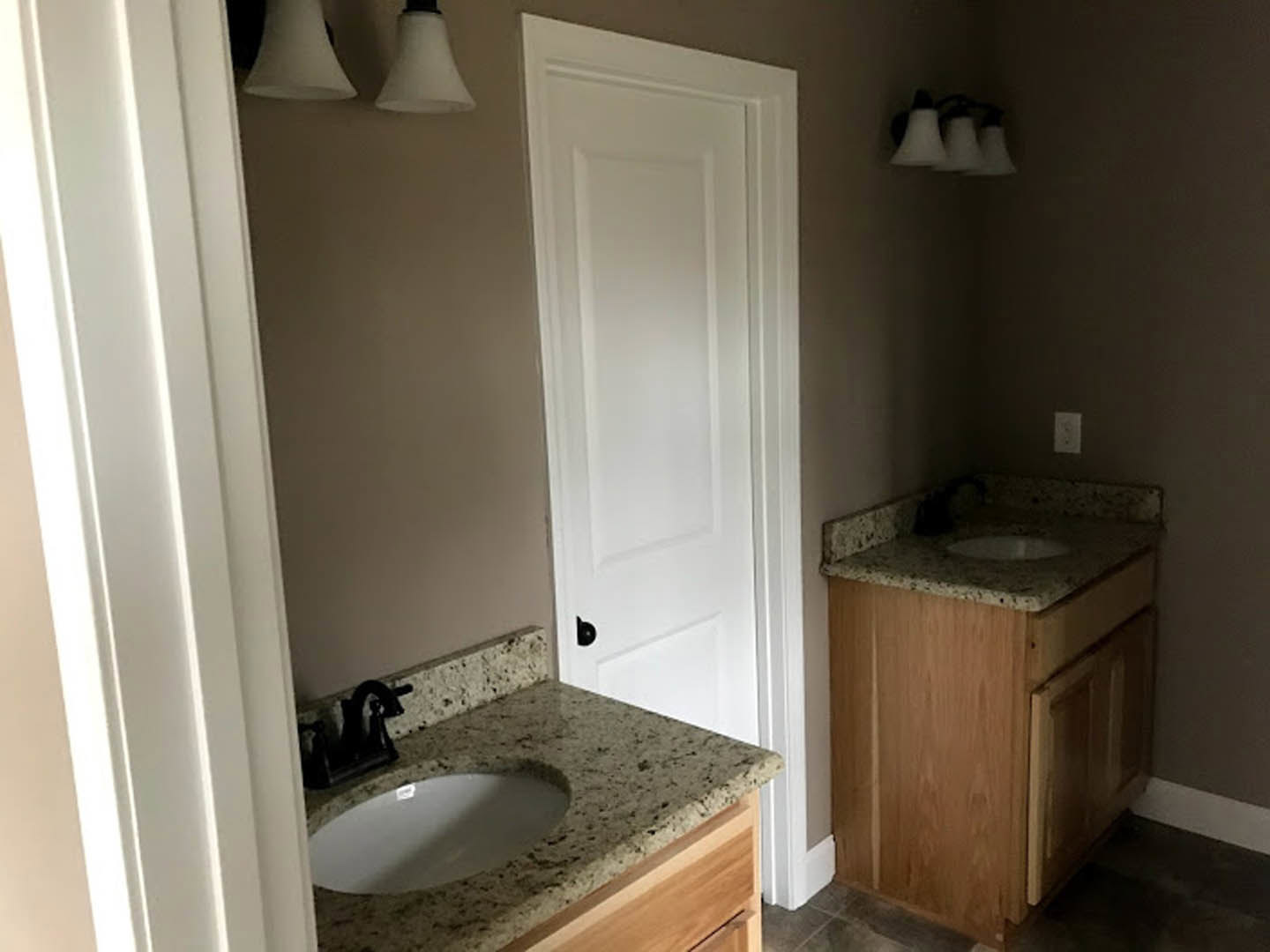 Double vanity bathroom with white sinks, chrome faucets, light wood cabinetry, large wall mirror, and modern white lamps above tile backsplash