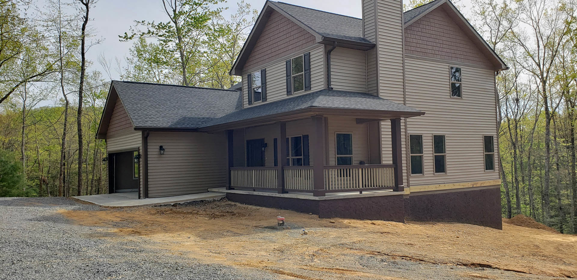 Two-story home with gray siding, white trim, covered front porch, concrete driveway, and multiple white-framed windows