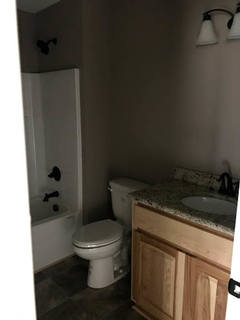Modern bathroom with white porcelain sink, chrome faucet, and toilet; light gray tile walls, wood vanity cabinet, and minimal accessories