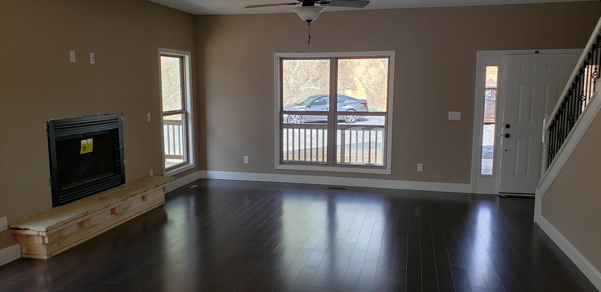Modern den with wood laminate flooring, black framed fireplace, large window overlooking parked car, light-colored walls, and wood planked baseboard