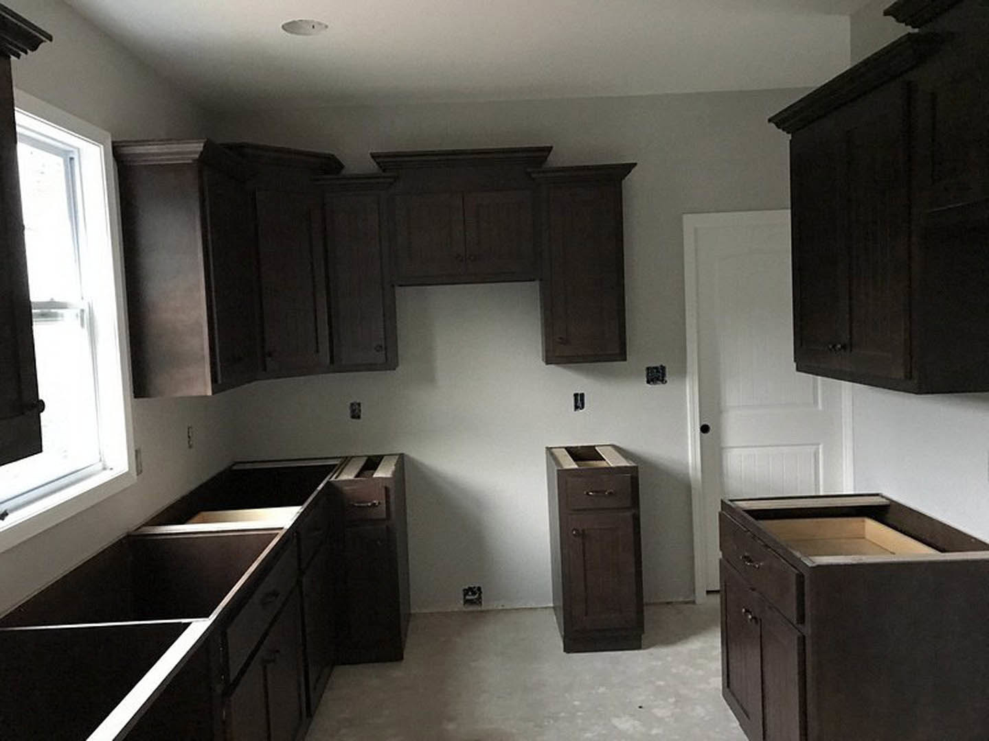 Dark wood kitchen cabinets with sleek hardware, open drawer revealing interior, grey flooring, sunlight streaming through window onto countertop