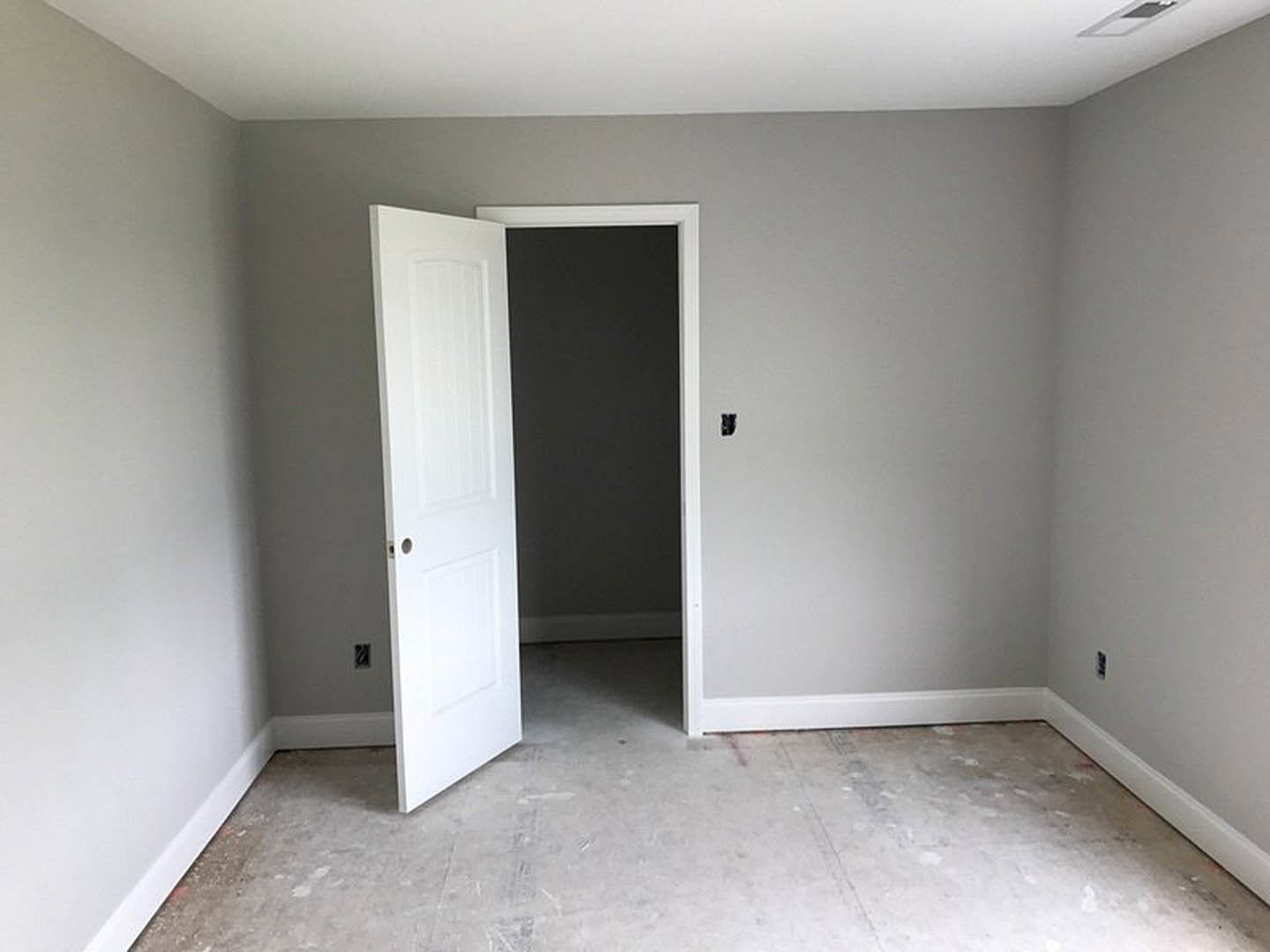 White door with round hole partially open in modern room, concrete floor, black accent wall with white trim, plaster ceiling