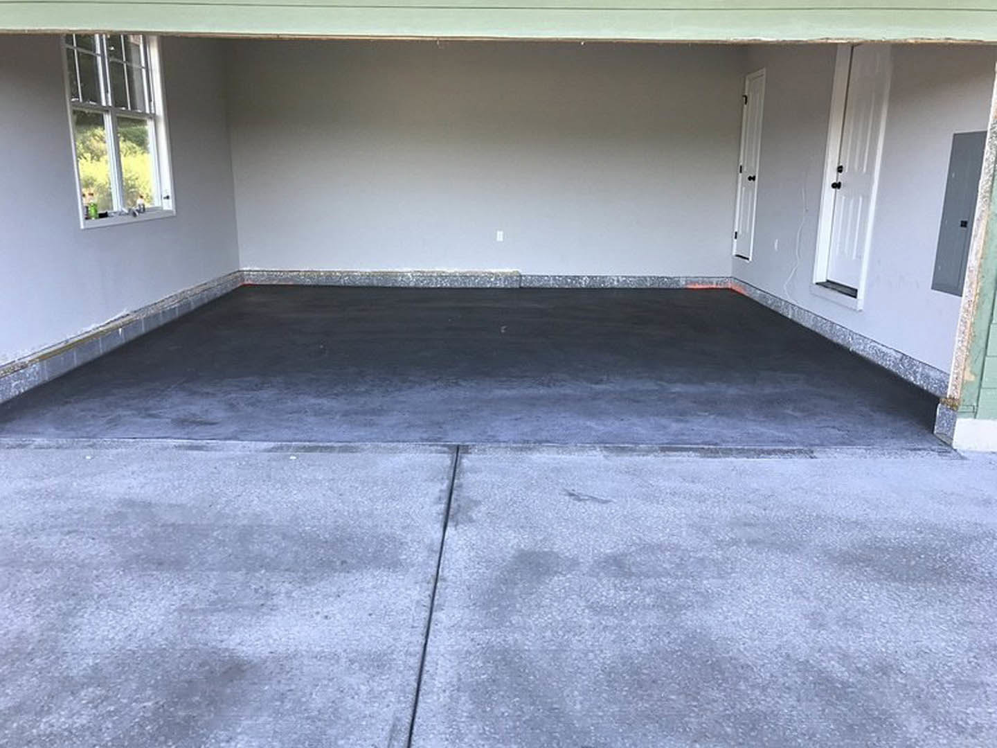 Garage with smooth concrete floor, white-framed window, white door, and white walls featuring a black square accent