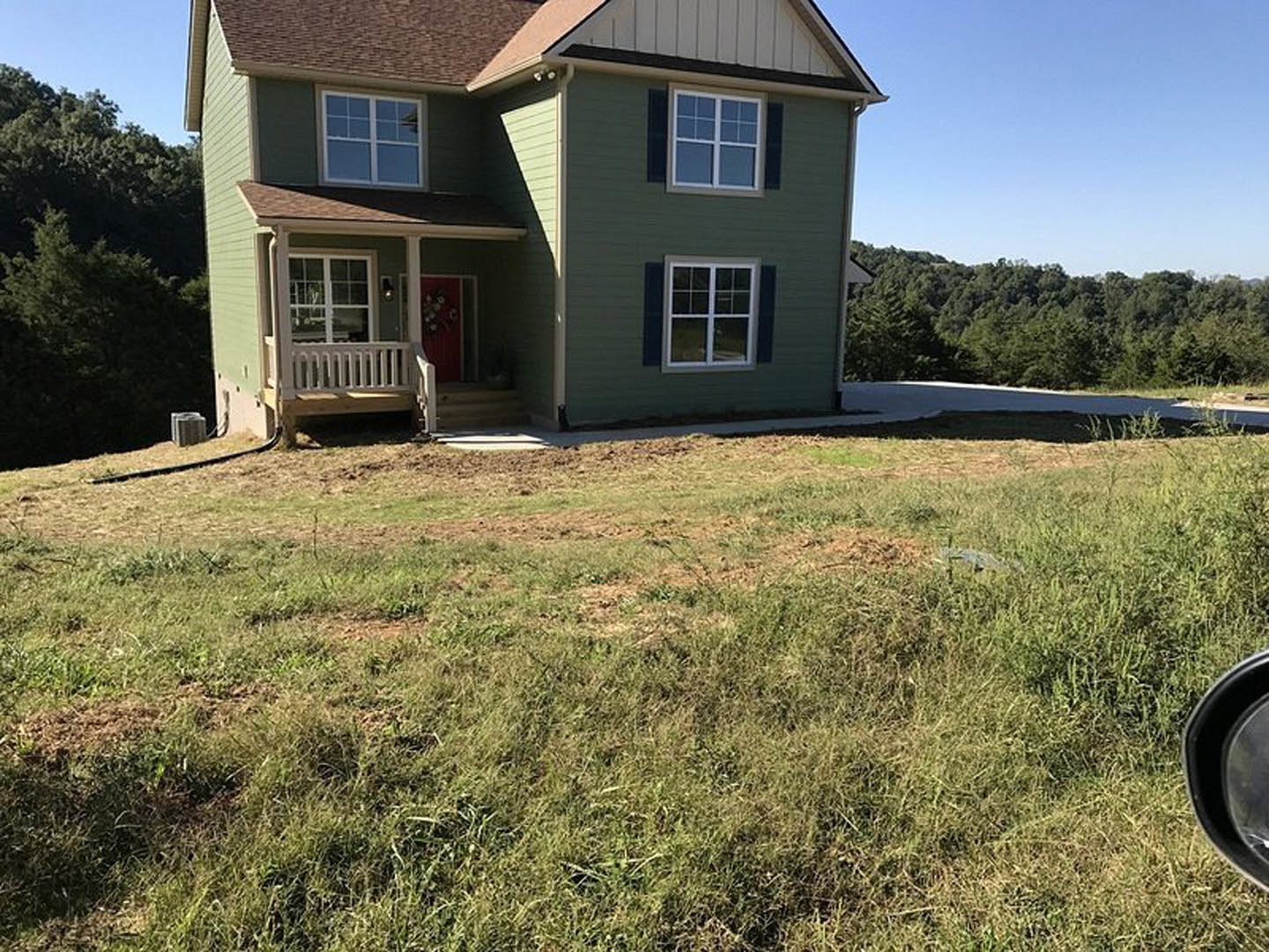 Green house with red front door, multi-pane windows, manicured lawn, mature trees in background, blue sky overhead