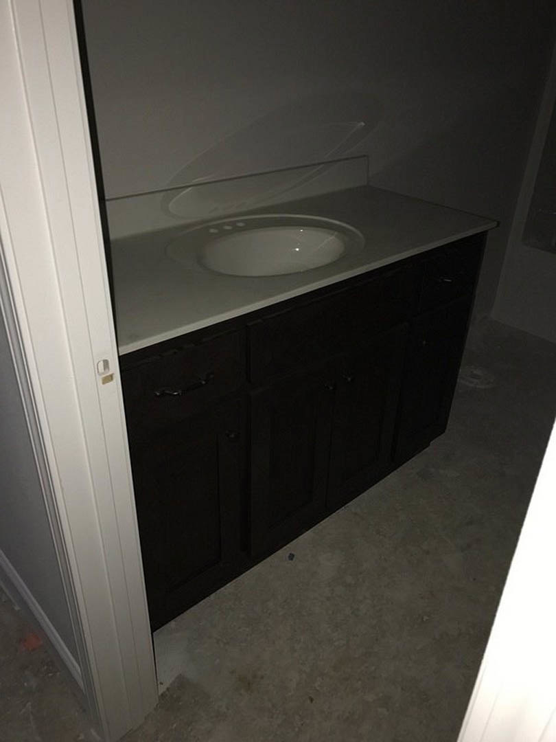 White ceramic sink with chrome faucet set in a light wood vanity, gray tile backsplash, and adjacent toilet bowl in modern bathroom.