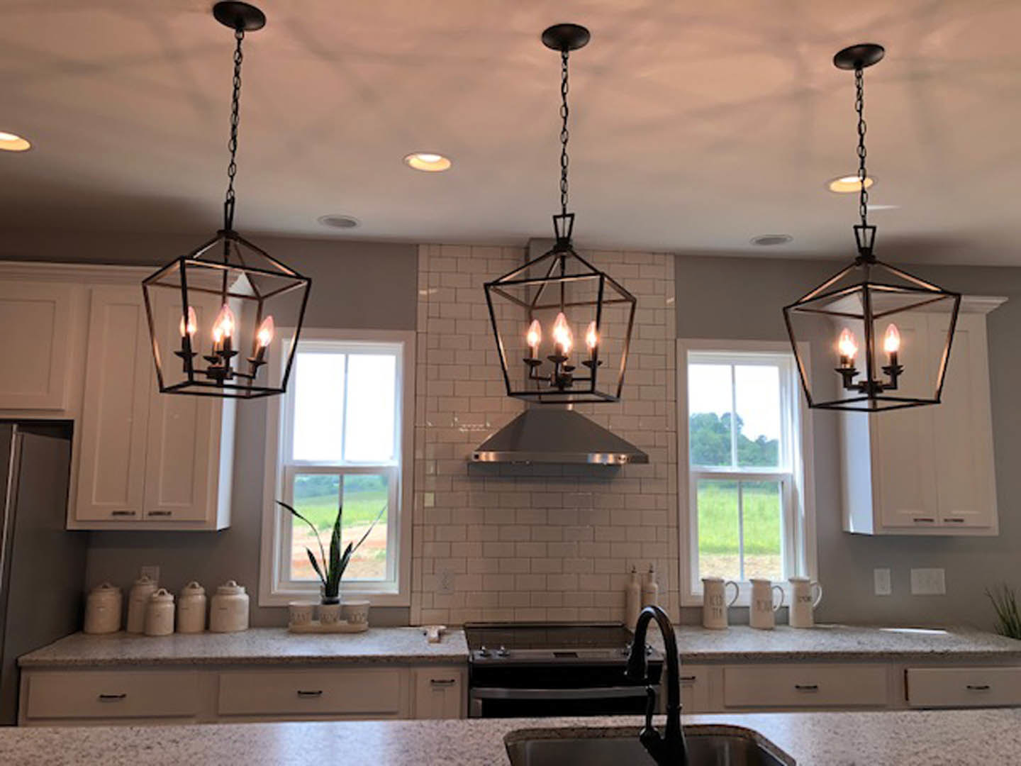 Spacious kitchen featuring a large central island with stone countertop, expansive window providing natural light, modern cabinetry, stainless steel sink, ceiling light fixture