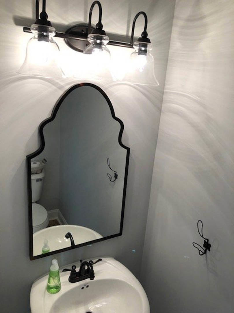 White bathroom sink with black faucet, rectangular mirror above, green soap bottle with white cap on countertop, light-colored wall in background
