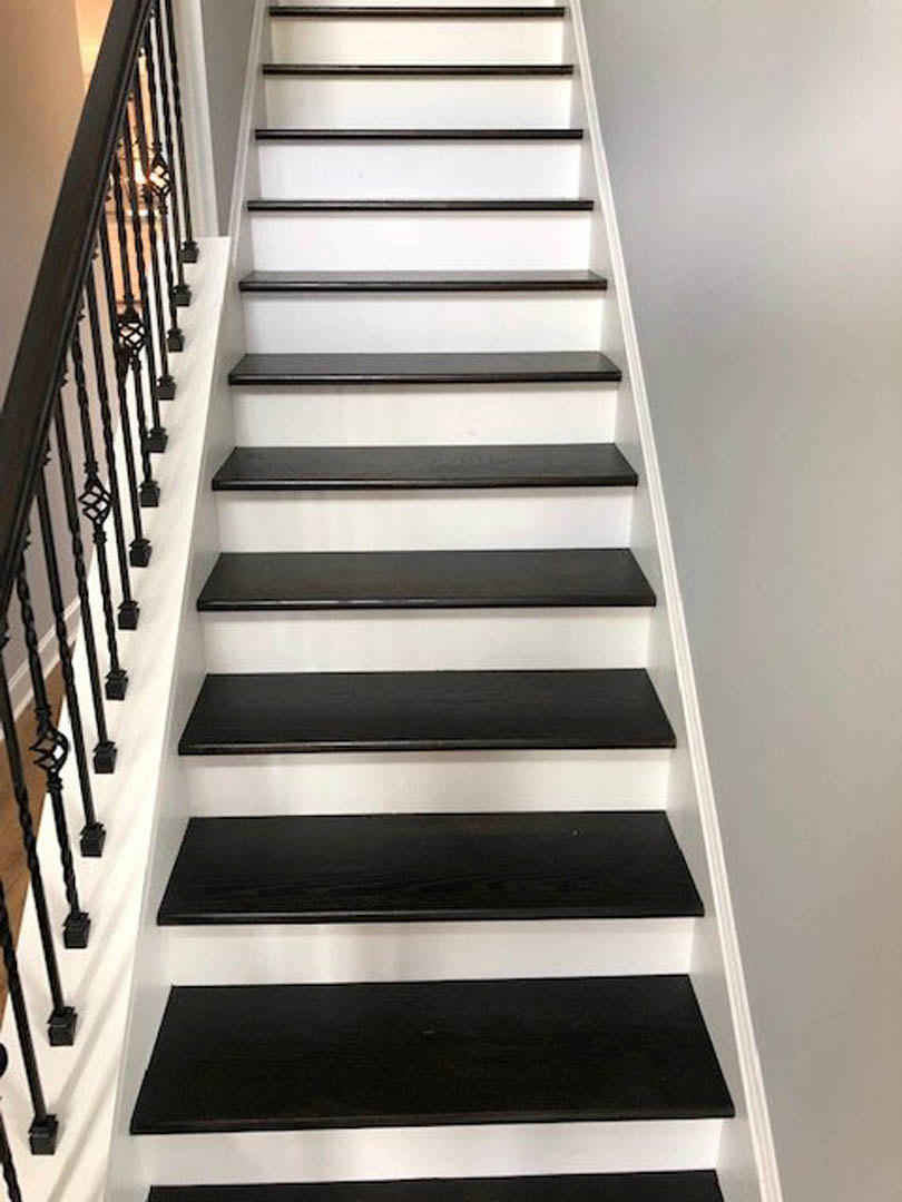Black wood staircase with white risers and balusters, modern handrail, white walls, symmetrical design