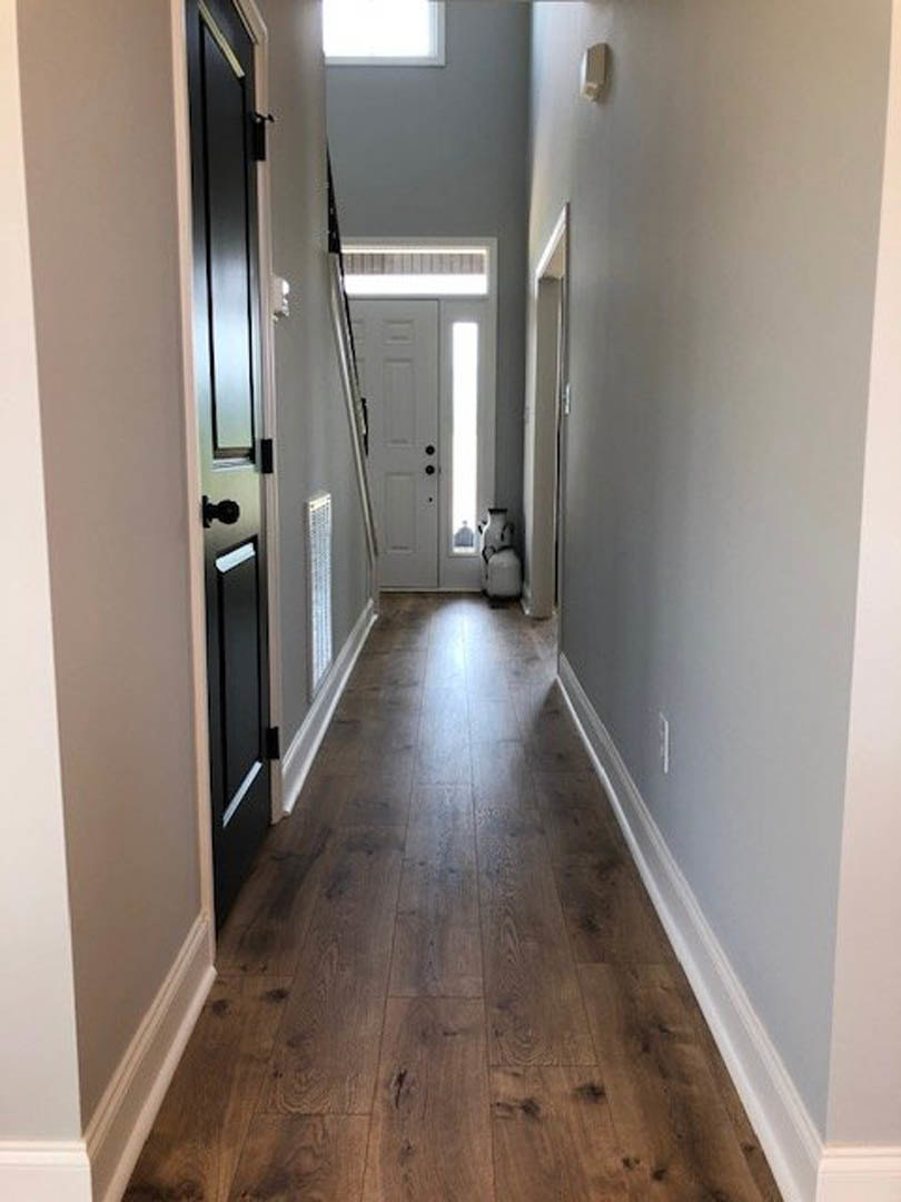Long hallway with light wood flooring, white walls, and a white door featuring black hardware