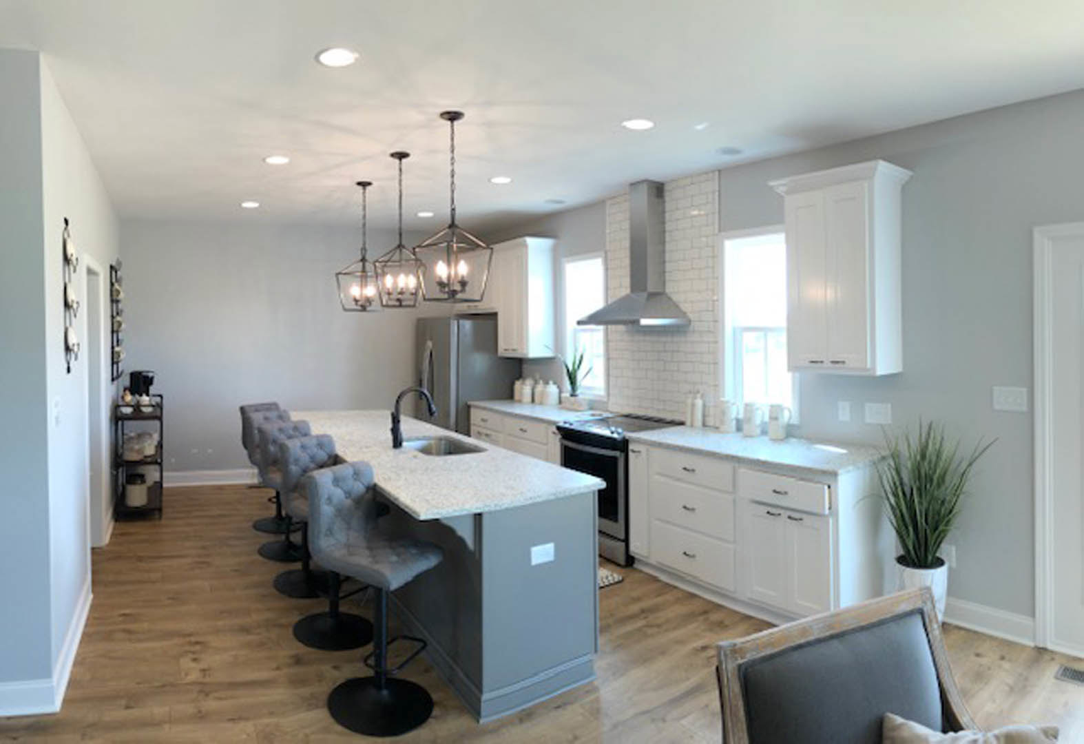Spacious kitchen featuring a large central island with barstool chairs, white cabinetry, stone countertops, stainless steel stove, pendant ceiling lights, and a potted plant on the