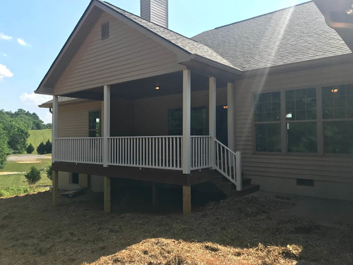 Two-story home with gray siding, covered front porch with white railings, manicured green lawn, multiple square windows, and white metal fence.