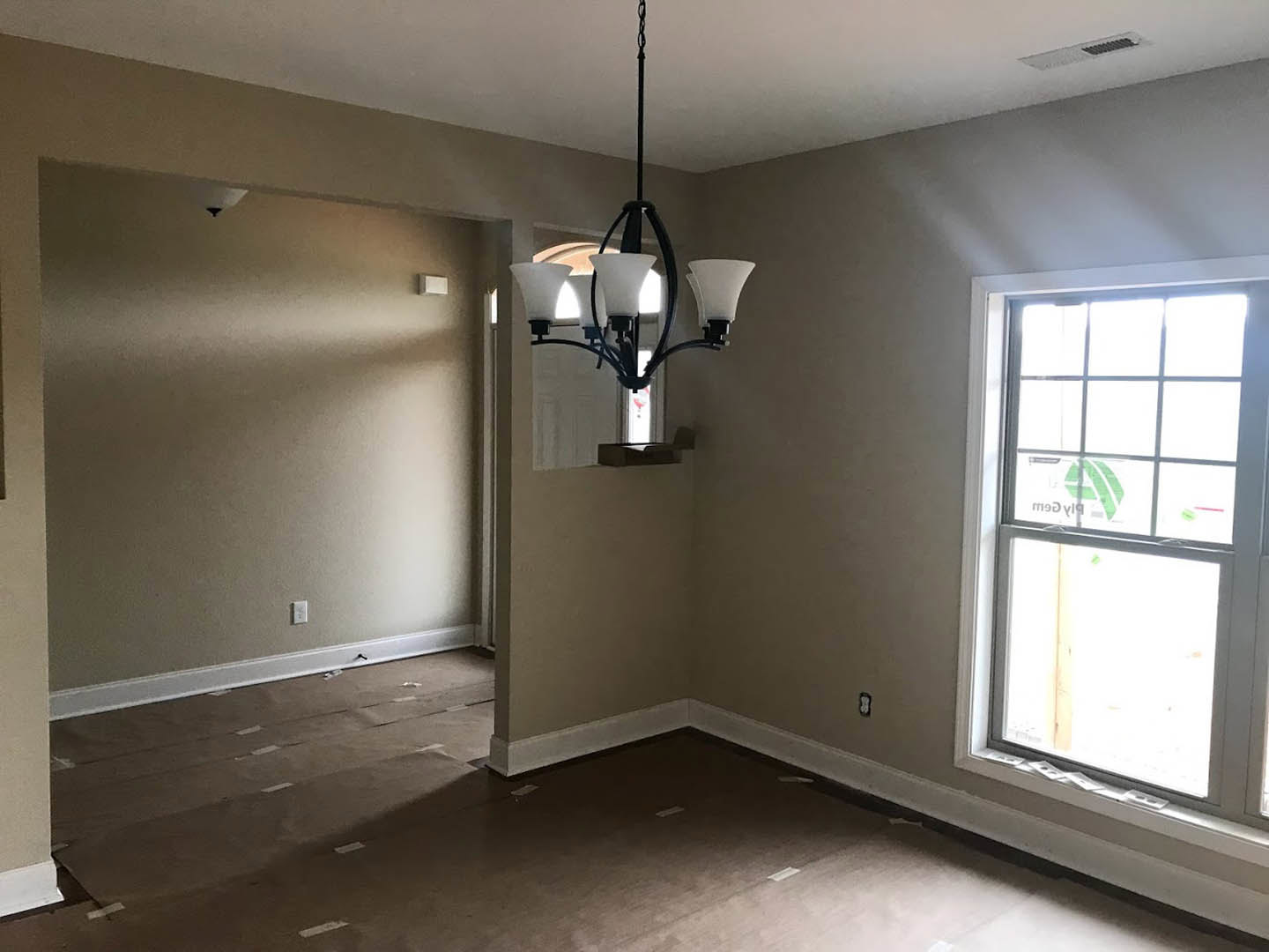 Corner of a plaster-walled room featuring a three-light chandelier, large window with sticker, and light-colored flooring