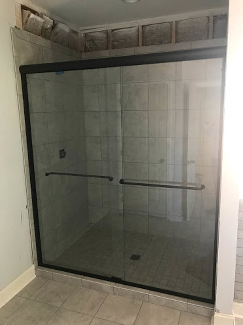 Glass shower door with matte black handle, tile floor in neutral tones, plaster walls, ceiling-mounted light fixture, metal towel bars on wall