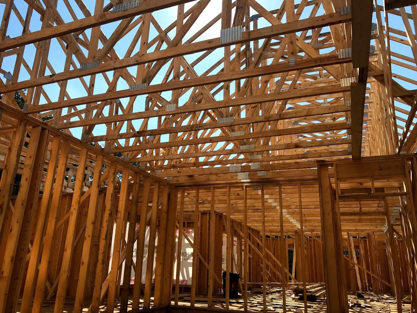 Exposed wood framing of a house under construction with beams and joists, set against a clear blue sky